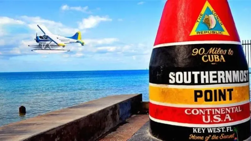 Seaplane flying above Key West Southernmost Point landmark.