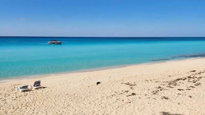Bimini beach with lounge chairs, turquoise water, and boat.
