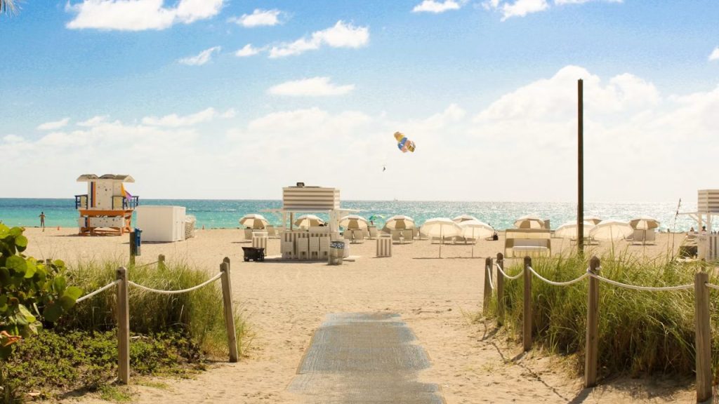Florida beach with umbrellas, cabanas, turquoise sea, and parasail.