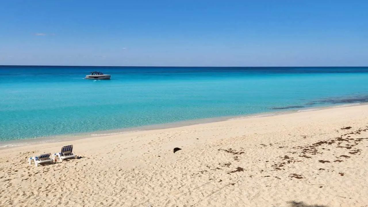 Bimini Beach with lounge chairs, turquoise water, and boat.