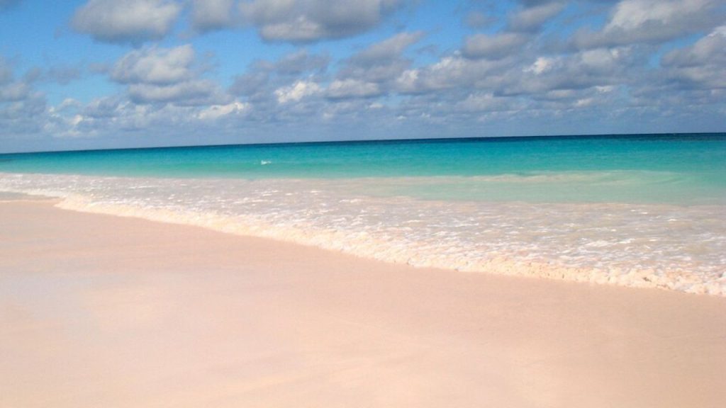 Pink Sand Beach with turquoise waves under partly cloudy sky.