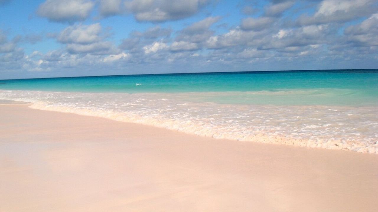 Pink Sand Beach with turquoise waves under partly cloudy sky.