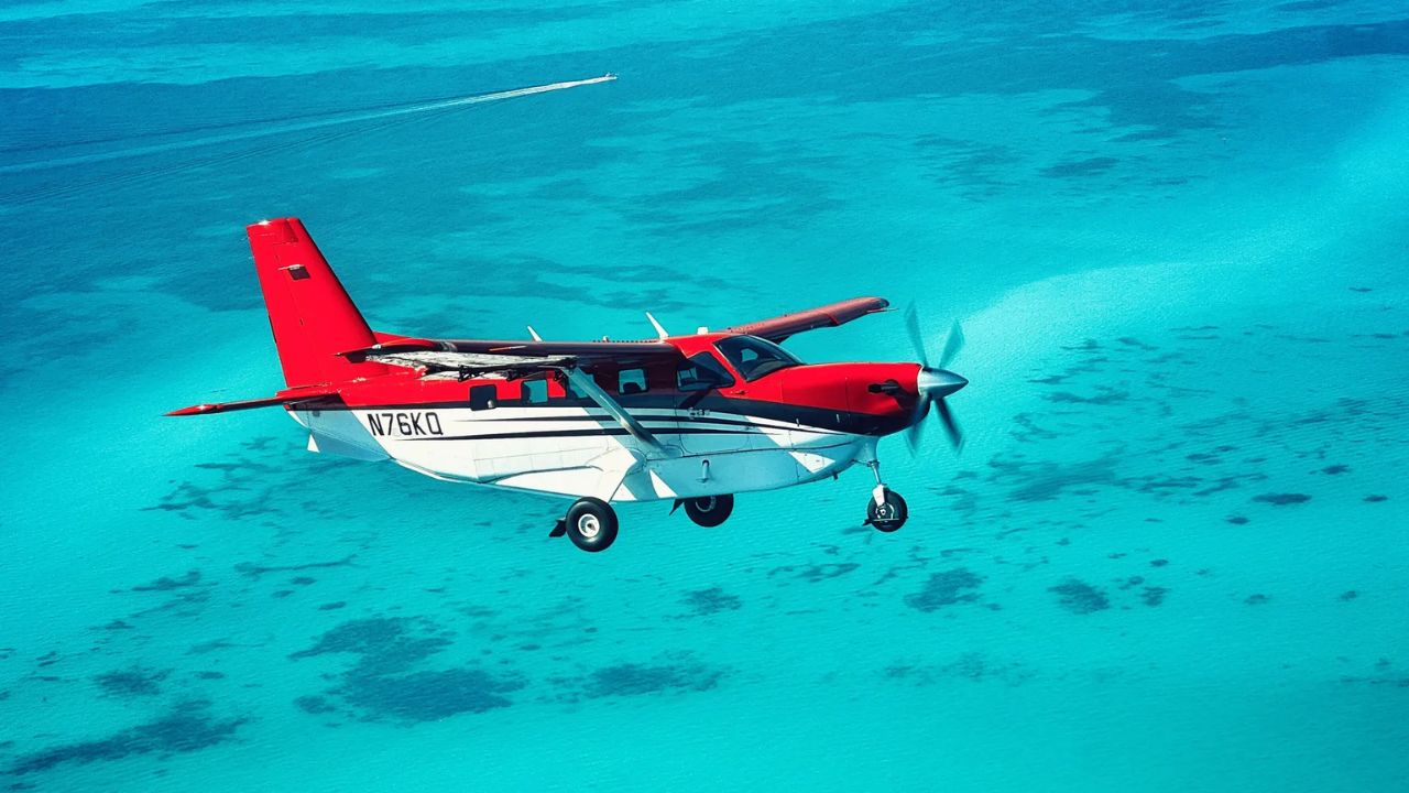Red and white seaplane flying above turquoise ocean
